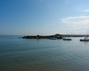 Obraz premium A serene, wide-shot photograph of a calm, blue sea and sky, featuring a short rock breakwater in the middle ground and small boats pedal boats anchored near the shore.