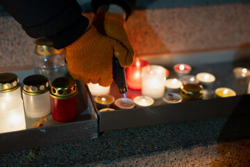 Close-up of a person lighting candles arranged on Krastmala steps using a torch lighter, showing warm glowing lanterns, textured stone surfaces