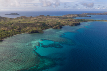 Aerial view of turquoise waters embrace the rugged coastline of the Yasawa Islands, where verdant hills meet the deep blue sea, Nadi, Western Division, Fiji.