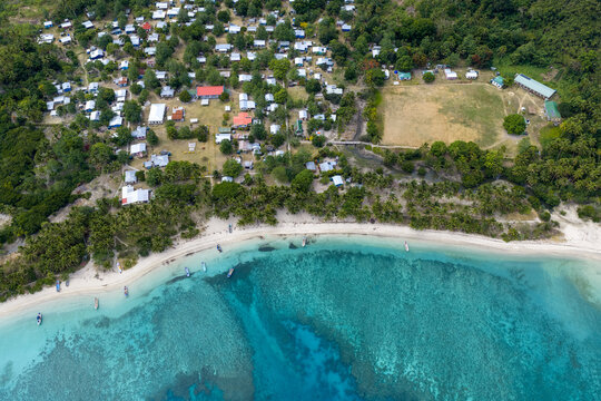 Aerial view of turquoise waters meet the sandy shore, fringed by a village nestled amidst lush greenery, Yasawas Islands, Nadi, Western Division, Fiji.