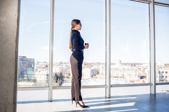 Businesswoman enjoying morning coffee while gazing at the city skyline from a modern office space in the early hours - Powered by Adobe
