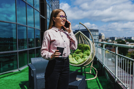 Woman enjoying the sunny rooftop while talking on her phone and sipping coffee in a vibrant urban landscape