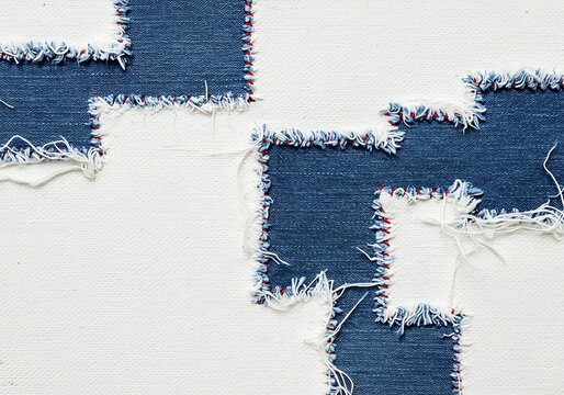 Denim fabric patches with frayed edges sewn onto white textile creating a rustic handcrafted patchwork design texture background
