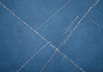 Durable blue denim textile close up with white decorative stitching creating an interesting fabric surface texture