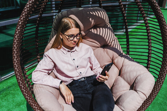 Relaxing in a cozy hanging chair on a sunny afternoon while browsing on a smartphone in a vibrant outdoor space