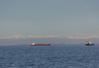 Cargo ships on calm sea with snowy mountains on the horizon