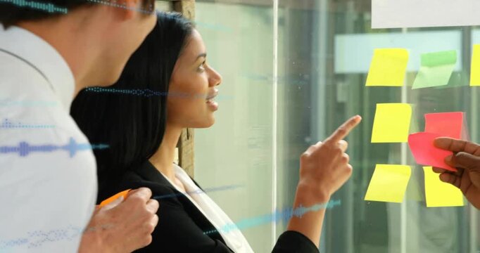 Woman speaking and pointing at yellow note on glass, man offering pad, overlay marking biz priority