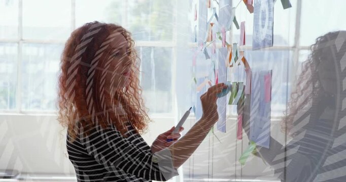 Woman sorting glass wall in design studio, lifting blue pad then sticking notes with animated glow