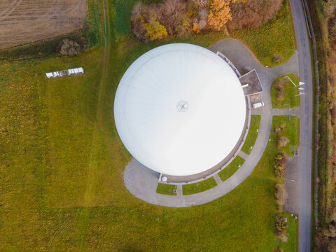 Aerial view of the spherical dome structure contrasting against the surrounding green fields and autumnal trees, Raisting, Bayern, Germany.