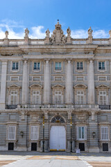 A detailed view of the Palacio Real's central entrance pavilion, featuring twin columns, a grand white doorway, ornate sculpture work, and the royal coat of arms at the rooftop.