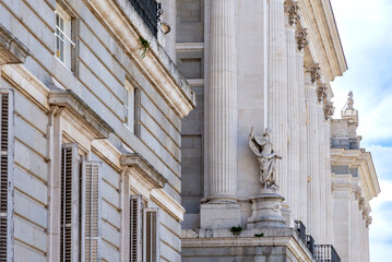 Close-up upward view of the Palacio Real’s ornate gray and white neoclassical façade, showing columns, statues, balustrade, and detailed windows against the sky