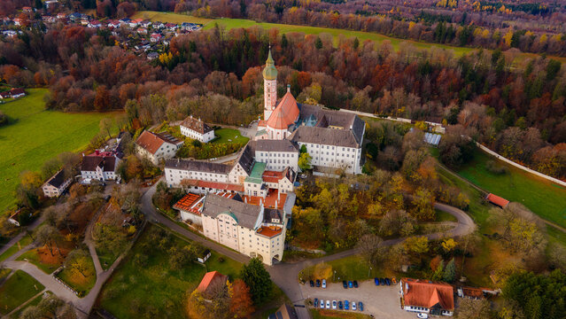 Aerial view of the Andechs Abbey complex, a beacon of white and red against the autumnal tapestry of surrounding forests, Andechs, Bayern, Germany.