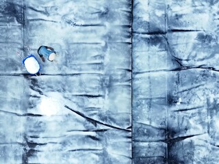 Ninh Hoa, Vietnam - 25 June 2025: Aerial view of bright white salt fields reflecting the sun, contrasted by the dark earth underneath and a worker with a blue bucket.