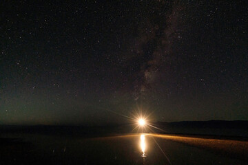 A starry night over the water surface, bright light illuminates the path to the Milky Way. The serenity and grandeur of nature in one shot
