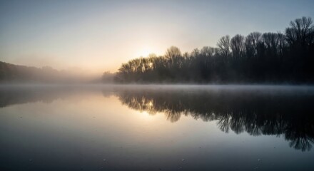 Obraz premium Misty sunrise over a still lake with tree silhouettes. Foggy morning with perfect reflections in the water. Atmospheric nature landscape background