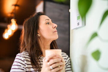 Beautiful happy woman push button digital thermostat at house