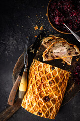 A luxurious Three Bird Wellington featuring layers of turkey, duck, and pheasant wrapped in golden puff pastry with herbed stuffing. Sliced to reveal the colourful cross-section and served on a rustic