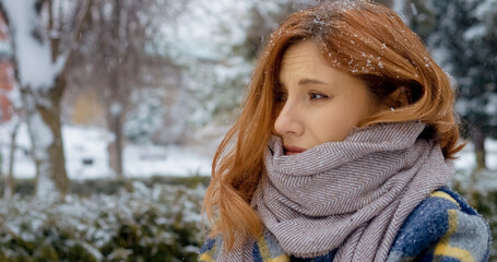A sick woman walks through a snowy park, sneezing and holding a napkin. The winter scenery includes falling snow and frost-covered trees, highlighting her discomfort.
