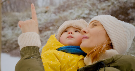 Obraz premium A mother holds her little boy while they delight in the snowfall at a park. They share joyful moments surrounded by winter scenery and playful snowflakes.