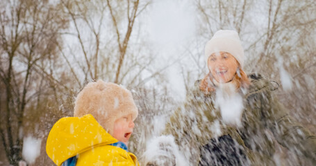 A mother plays joyfully with her young son in a snowy park. They throw snow at each other, laughing...