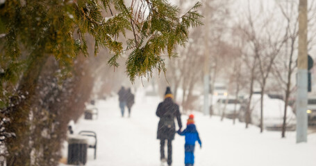 Snow falls steadily over the urban landscape, covering streets and trees, as families walk hand in hand, enjoying the winter atmosphere and challenging conditions.