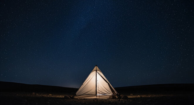 Illuminated Tent under a Deep Blue Night Sky Filled with Bright Stars and Milky Way
