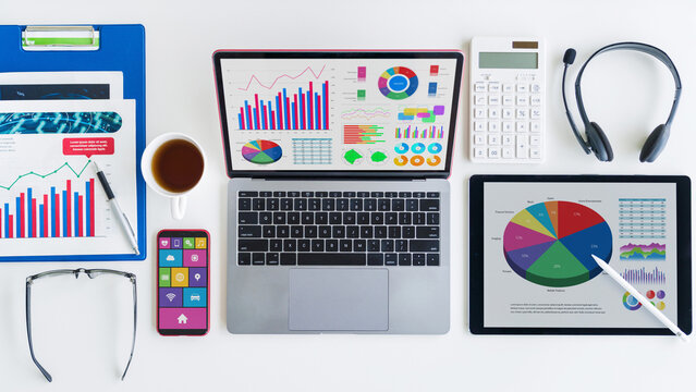 Professional modern workspace with financial charts on laptop, tablet, and documents, coffee, phone, calculator, and glasses for business analysis.