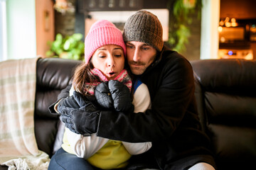 Fototapeta premium Portrait of a frozen couple sitting frustrated on the sofa in the living room in winter outerwear at home and trying to keep warm.