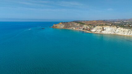 Aerial view of the turquoise and crystalline sea. On the horizon, on the background, there is a promontory. Tropical panorama.