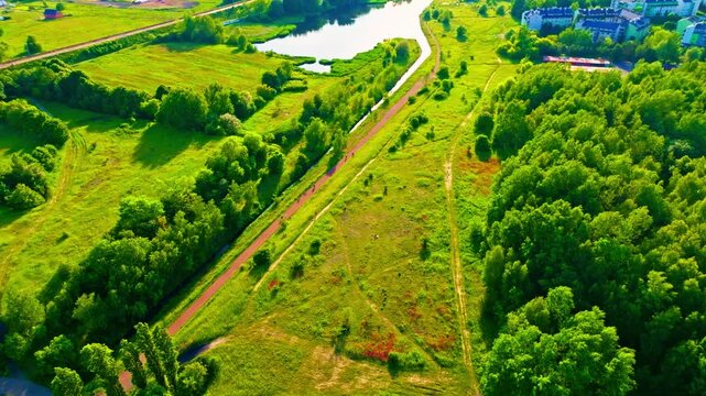 4K aerial flight over a scenic nature area with pond, paths, people walking dogs, cycling and enjoying outdoor leisure.