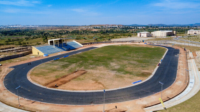 Aerial view of a stadium with a running track and vibrant green field, surrounded by buildings and open land, Barakin Naraguta, Plateau, Nigeria.