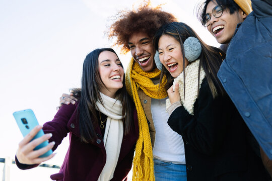 Diverse group of teenage friends having fun taking selfie portrait at city street on winter. Holiday lifestyle and technology concept