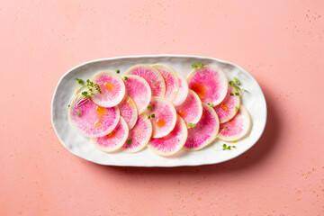 Fresh watermelon radish thinly sliced, adorned with delicate microgreens. Pink background. Top view.
