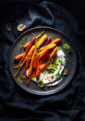 Warm salad with roasted carrots and labneh. Dark background. Top view.