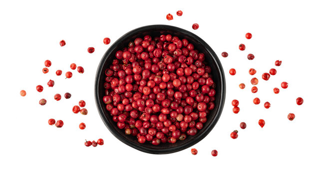 Pink peppercorn  pepperberry  in black bowl flying isolated on white background. Aromatic spicy ingredient for cuisine