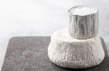 Soft cheese wheels, artisanal presentation on stone board. Grey background. Close up. Copy space.