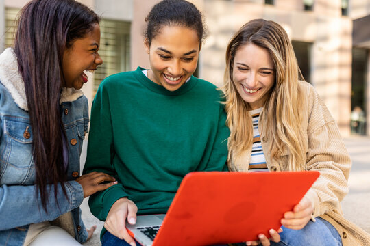 Three diverse student friends are sitting side by side using a laptop, focusing on learning together at the university campus. Collaboration, teamwork, and academic education concept.