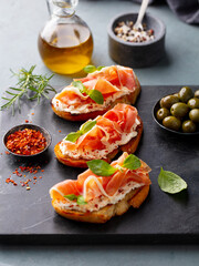 Crispy bruschetta topped with jamon, creamy cheese and fresh basil leaves. Grey background.