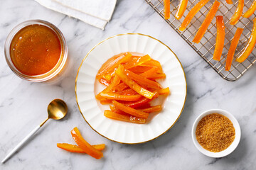 Candied orange fruit peel on white plate with jam. Marble background. Top view.
