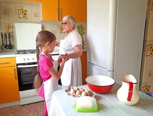 A grandmother and her granddaughter set out the necessary ingredients for cooking on the table.