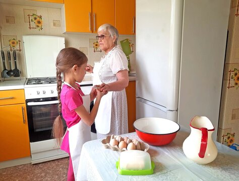 A grandmother and her granddaughter set out the necessary ingredients for cooking on the table.