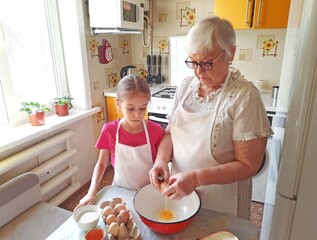 A grandmother and her granddaughter are making pancakes in the kitchen.