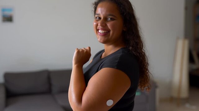 Happy young african woman smiling on camera with diabetes patch on arm at home - Disease, hyperglycemia and health care concept 