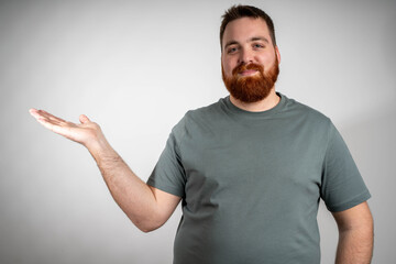 Smiling young ginger man pointing with hand at copy space isolated