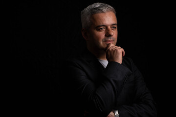Thoughtful businessman posing with hand on chin in low key chiaroscuro portrait
