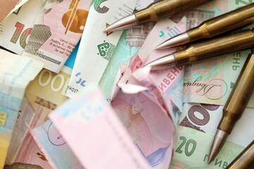 Many rifle bullets lies on lots of ukrainian money bills close up