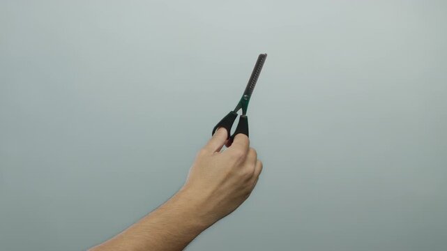 Caucasian man's hand holding scissors against a blank white wall background, emphasizing simplicity and isolation.