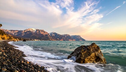 Rocky beach with mountains in distance, water swirling, blue sky and clouds