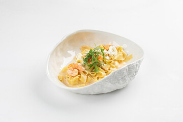 Tagliatelle pasta in creamy sauce with shrimp, herbs and cheese served in a textured white designer bowl on a white background