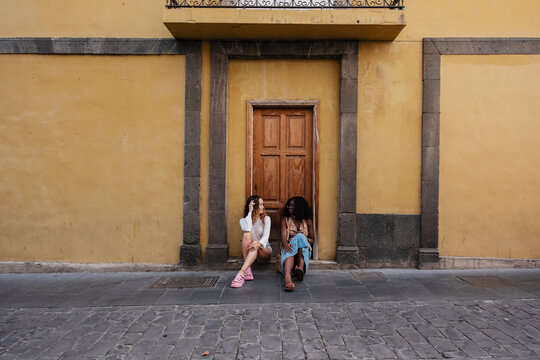 Diverse women friends sitting discussing against yellow wall